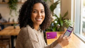 Pessoa brasileira segurando cartão Nubank magenta e celular com app de controle financeiro em fundo residencial desfocado
