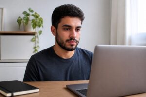 Young Brazilian man looking at a laptop while studying online at a table